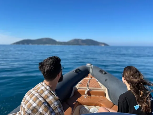 Zwei Personen auf einem Boot, das auf eine Insel am Horizont zufährt