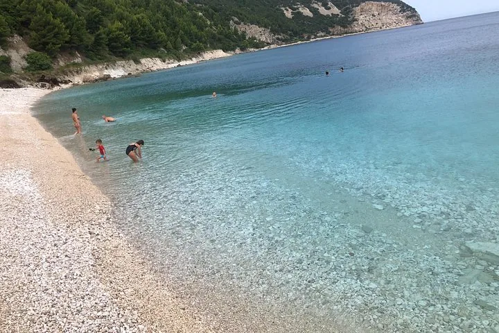 Persone che camminano nell'acqua e nuotano in acque basse e cristalline su una spiaggia di ciottoli