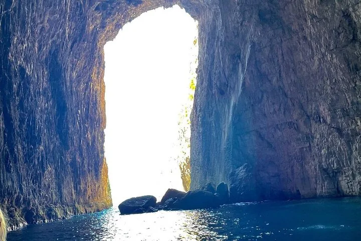 Vista dall'interno di una grande e alta grotta marina verso la luce intensa del sole