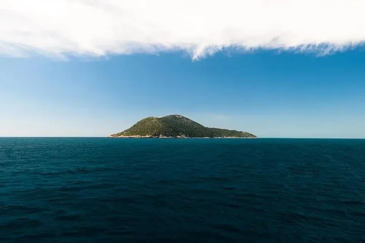 Eine kleine grüne Insel, die aus dem tiefblauen Meer unter blauem Himmel emporragt